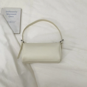Close-up of cream lychee leather texture and metal buckle on minimalist shoulder bag