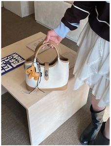 Close-up of beige tote bag featuring metal twist lock and yellow horse charm detail