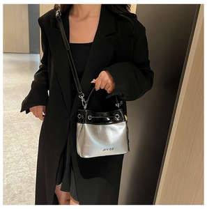 Detail of a silver and black bucket bag with adjustable strap worn on a black coat