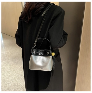 Detail of silver bucket bag with black trim worn over a black coat in a stylish setting
