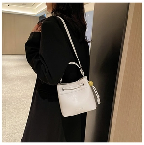 Detail of white bucket bag with PU leather texture, drawstring closure and ball pendant