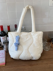 Chic cream quilted tote bag with blue bow charm on a wooden table, minimalist spring style