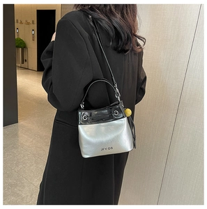 Fashionable silver bucket bag with black handles and yellow charm on a female model