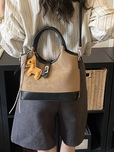 Brown suede tote bag with black leather trim and horse charm carried by a woman