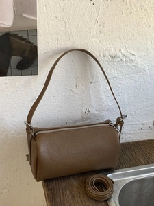 Brown lychee pattern cylinder handbag with dual straps on a minimalist wooden surface