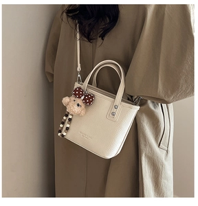 Detail of beige lychee leather bucket bag with embossed logo and plush bear charm