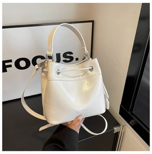 Detail of white glossy bucket bag featuring sleek top handle and detachable shoulder strap