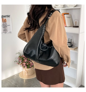 Model wearing a black leather tote bag with silver eyelets in a home interior setting