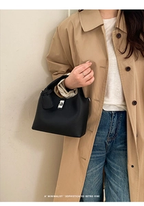 Detail of black lychee grain leather bucket bag with silver lock and pendant on model
