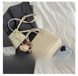 Detail of beige lychee leather bucket bag with decorative pom-pom and adjustable strap