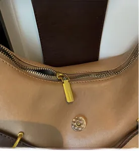 Close-up of smooth gold zipper and magnetic snap closure on beige leather tote bag
