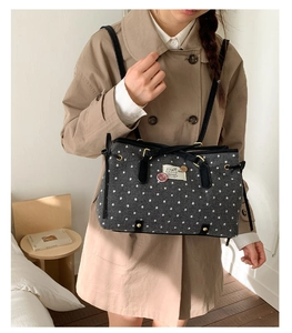 Detail of grey polka dot tote bag with black leather handles and vintage brand label