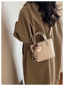 Detail of beige bucket bag with litchi texture, logo embossment and plush bear charm
