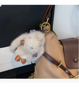 Detail of grey plush rabbit charm with golden ring on a leather tote bag strap