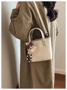 Detail of cream bucket bag in pebble leather with plush bear charm and printed logo