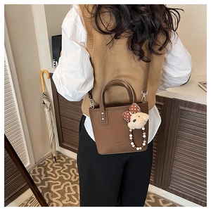 Detail of dark brown leather bucket bag with plush bear charm worn as a crossbody