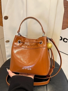 Caramel brown drawstring bucket bag in glossy leather texture with adjustable shoulder strap