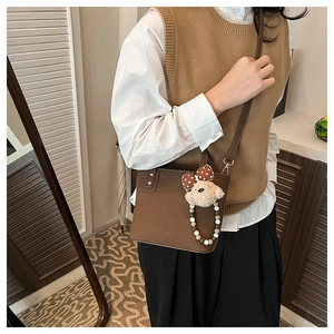 Detail of dark brown leather bucket bag with plush bear charm and pearl chain accent