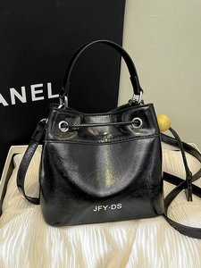 Glossy black bucket bag with adjustable strap and top handle on a white textured base