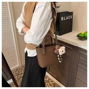 Detail of dark brown litchi pattern bucket bag with cute plush bear charm on a model