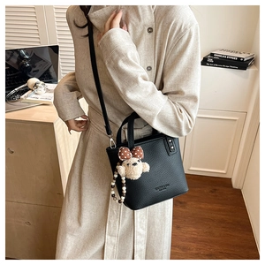 Detail of black pebbled leather bucket bag featuring a teddy bear charm and pearl strap