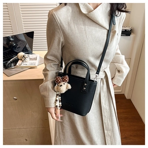 Détail du sac cabas en cuir grainé noir avec charme ours en peluche sur modèle en manteau