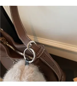 Detail of brown leather handbag featuring silver metal rings and a white plush pompom charm