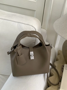 Elegant khaki bucket bag with lychee texture and silver twist lock on white sofa