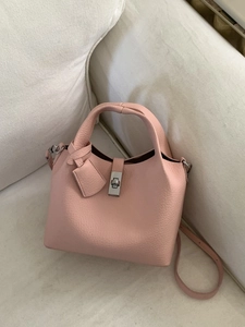 Pink lychee grain leather bucket bag with silver lock and shoulder strap on a white sofa
