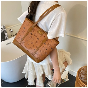Détail d'un sac cabas marron avec motifs d'ours et plaque dorée porté par un mannequin