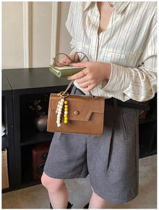 Detail of a brown faux leather shoulder bag with ethnic beaded charm and round snap closure