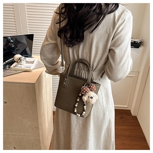 Model view of a dark brown pebble leather bucket bag with a cute teddy bear pendant
