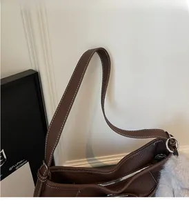 Close-up of brown leather handbag with white stitching and grey plush keychain charm
