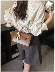 Close-up of textured brown leather crossbody bag with vintage buckle and beaded charm