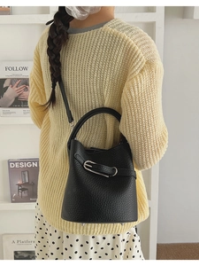 Model wearing a black lychee pattern leather bucket bag with adjustable strap and buckle