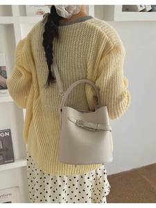 Close-up of beige lychee grain bucket bag worn by a model in a cozy lifestyle setting