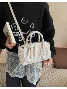 Close-up of pleated cream handbag with golden zipper and slim shoulder strap
