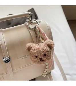 Macro shot of a light brown plush bear charm with woven lanyards on a checkered tote bag
