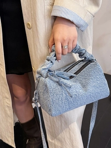 Sac polochon en jean bleu avec poignée plissée et bandoulière amovible porté par un modèle