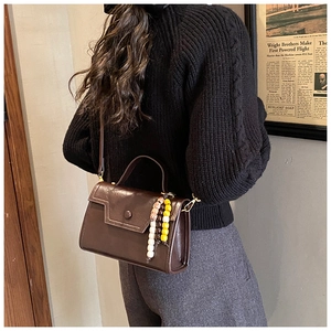 Side view of vintage brown crossbody bag with colorful bead charm on a model's shoulder