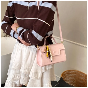 Detail shot of light pink square crossbody bag with a colorful beaded tassel charm