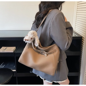 Detail view of khaki pebbled leather shoulder bag with a cute white rabbit keychain