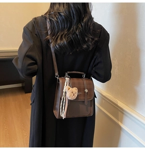 Detail of dark brown vintage faux leather handbag with embossed texture and plush bear charm