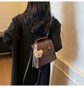 Detail of coffee brown faux leather bag with adjustable strap and cute plush bear charm