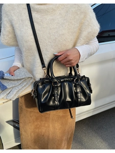 Detail of black pleated crossbody bag with dual handles and gold hardware accents