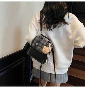 Detail of grey plaid mini backpack with plush bear charm worn by a model on stairs