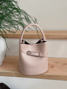 Pink pebbled leather bucket bag with silver metal buckle on a minimal wooden stand