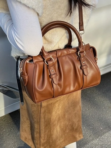 Brown ruched leather handbag with gold hardware and adjustable strap in minimalist style