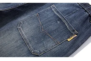 Detail of dark blue washed denim jeans featuring elastic waist and yellow design label