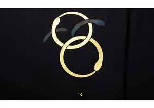 Détail des anneaux de serpents entrelacés et texte doré sur le tissu noir du t-shirt